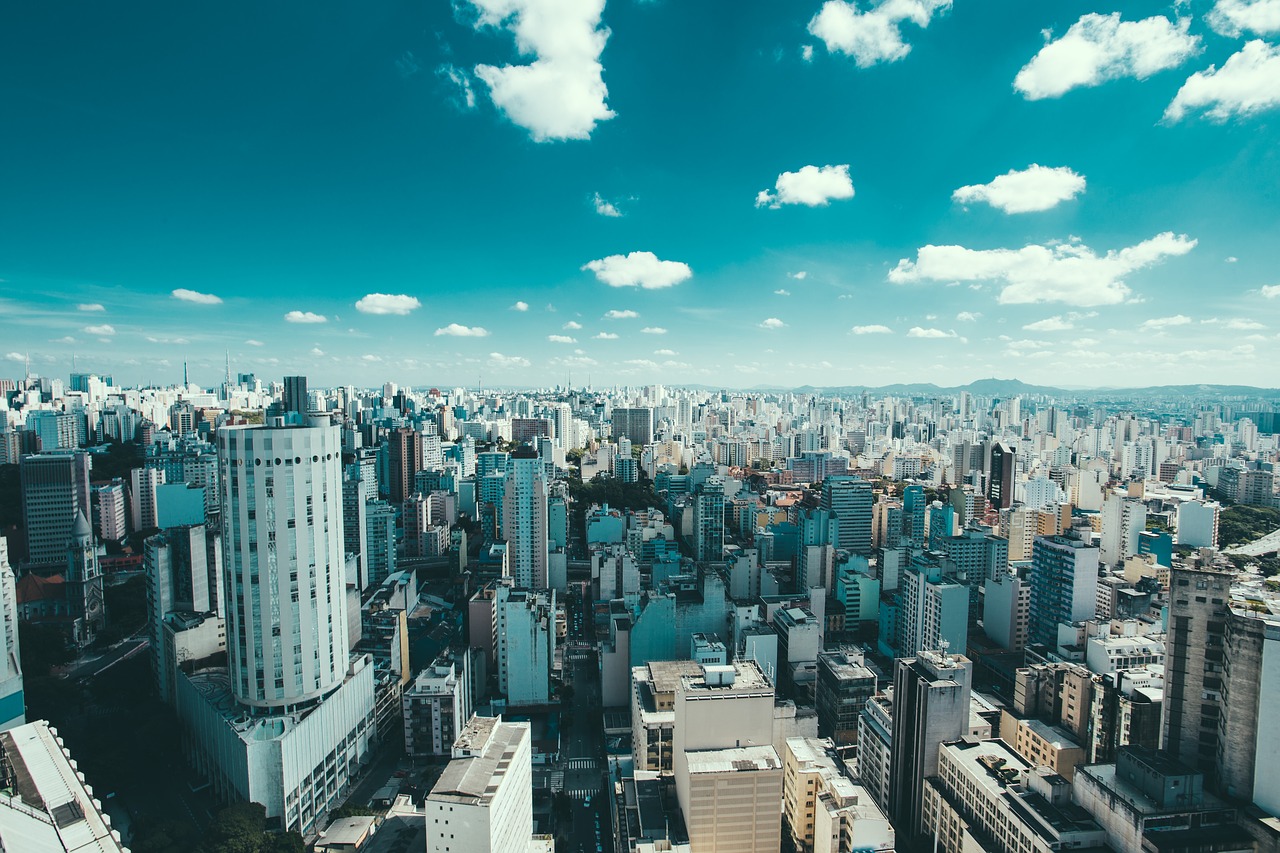 Foto de vista aérea da cidade de São Paulo. Céu está azul com poucas nuvens.